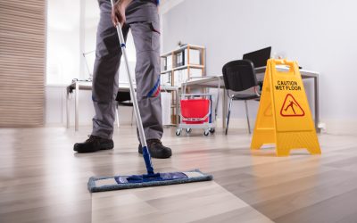 Low Section Of Male Janitor Cleaning Floor With Caution Wet Floor Sign In Office