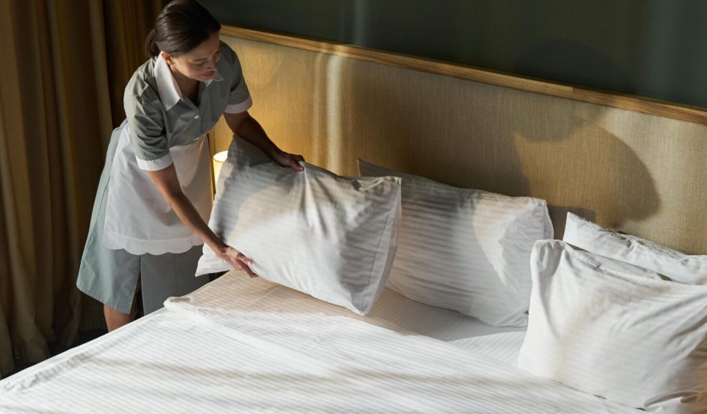 Housekeeper adjusting pillows and making bed in a modern hotel room. Neatly arranged white linens create a clean and welcoming atmosphere SSUCv3H4sIAAAAAAAACnxUPY/cIBDtI+U/rFwfCp82pEyRLlL6KMUA41t0XrMy9kVRdP892F47eLWXDt4w8x7DG/58/HA6VRZScNXn0595l/eh66Y0DjCG2GeYPt3wAXuPQ4m8DqKmJQCh3KEPYxwCdCVoYXTnHi6YwX7quhl+W4JVGmGcEqZCC3Rw+Z33Ymfw0WIao3sp0XSexhGHHS+KOhjxOas4lN2u/GPdn7bAEswZOVR9x3jtsLpRrDSTnSPfsK82dGV5p8QXhGn8/ekrpPPcy0elQnLYddBjnNK/ouvi537pZ+zd3Iad4/7G+0VySB6ION/LbvXu21gmM8rqhxl+QLikMSwPV2Y06sCn9aNsG54Xtus5jvGuwCH9y5RCjyk9FH0zQ5nslfUNByTOUEpk4w2x3AjikbXGeU0lMwcC0VonbUuJsA0nEpqWaONqgoIzbxtssKX/yNfFW+GnATuE1aQ3HRUK8M4JTkyDnsi61gQUKtIyDq52isl211Bxxig6SQlHjUQqOwu2lDgnWyfBcqfWDq4Xr15+5We+LOa9KYDJh1iY+TU66NKd7SFcYYBD3nUILvTPBRLH8zLQWyUXp34c5hbvj1J1MV7B5kH4fGozDW74GVLKx/2GlyOXv494KXj6OC4Nu1WtfJ7JecuEMLypheZUcWmM4VX5E5xDrrPI2QRO1y6CR38Yhc0WrJGaa6Zq/Y7P1wOSc/n03hytR2pl5O3l9x9mspeQT/6PmlOp/kutqCy0PaQ2jdioDz9jPhP8o5+xUpBNr7LlpZOOSN/WBFohiZeGaVTArN9/saOoiilaU2q0pPuBO1EVr0UeJ6a1WEx50xPmNlSohKZCG2KUZtn3uiG2AZfNz6mgIJuGu5z19hcAAP//AwDWlHiDZwYAAA==